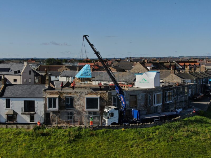 A truck crane lifts a prefab loft conversion up onto a roof.